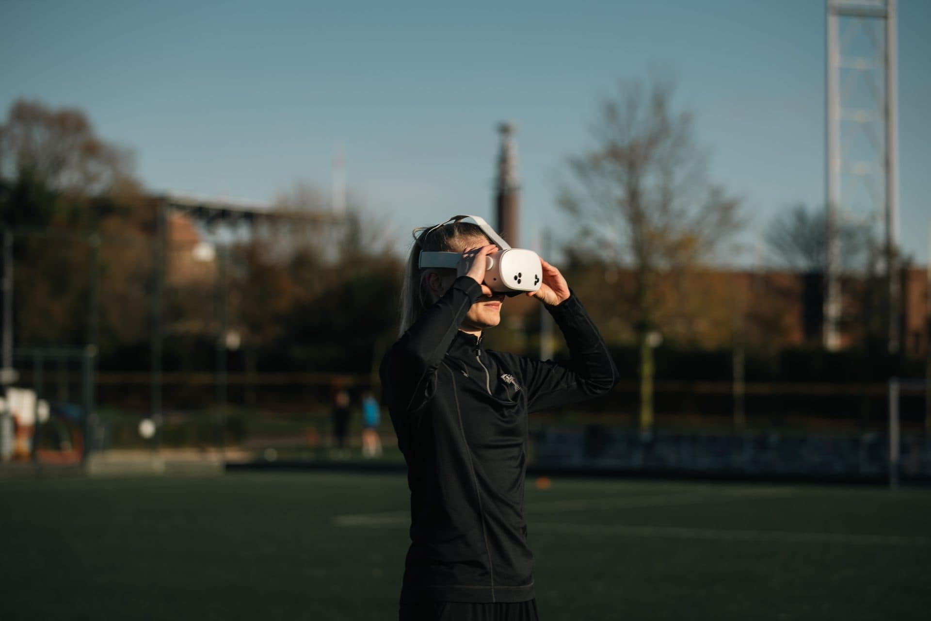 A football player wearing a headset trains on a floodlit pitch at dusk